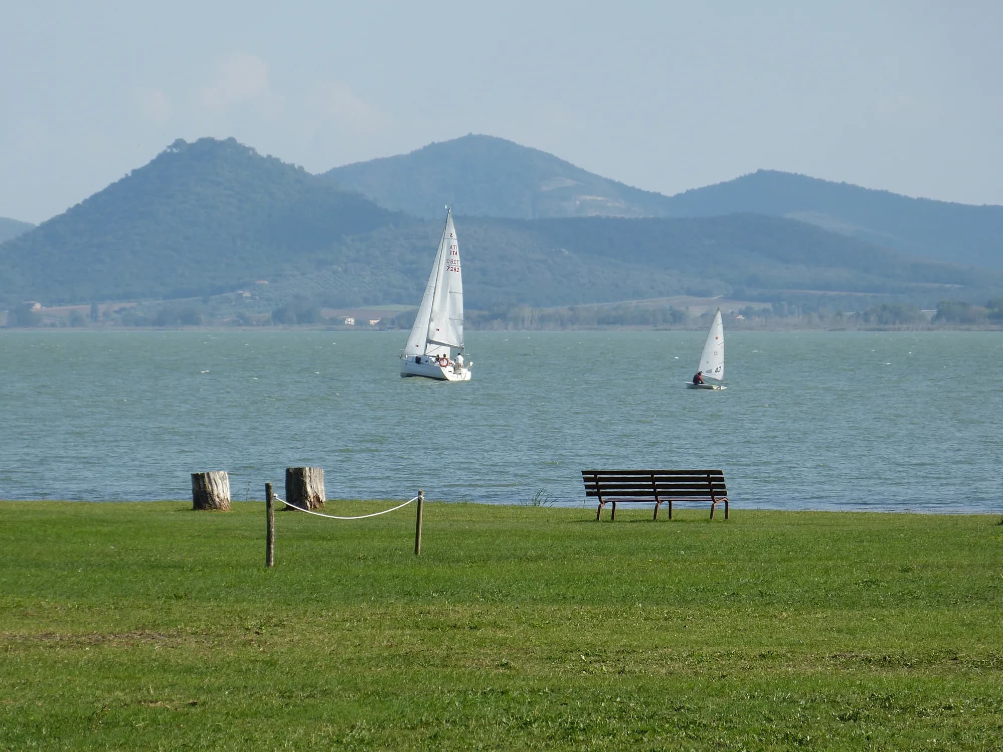 Voiliers sur le lac Trasimène à Castiglione del Lago, avec les collines en arrière-plan et une pelouse au premier plan