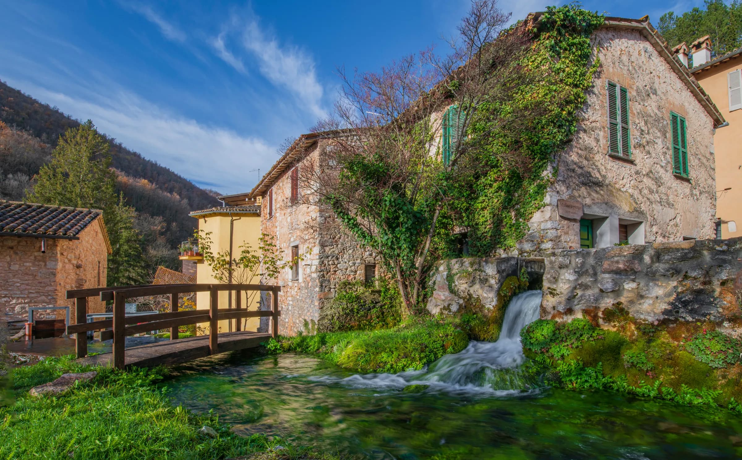 Case in pietra, un ponticello di legno e una cascatella tra i canali di Rasiglia