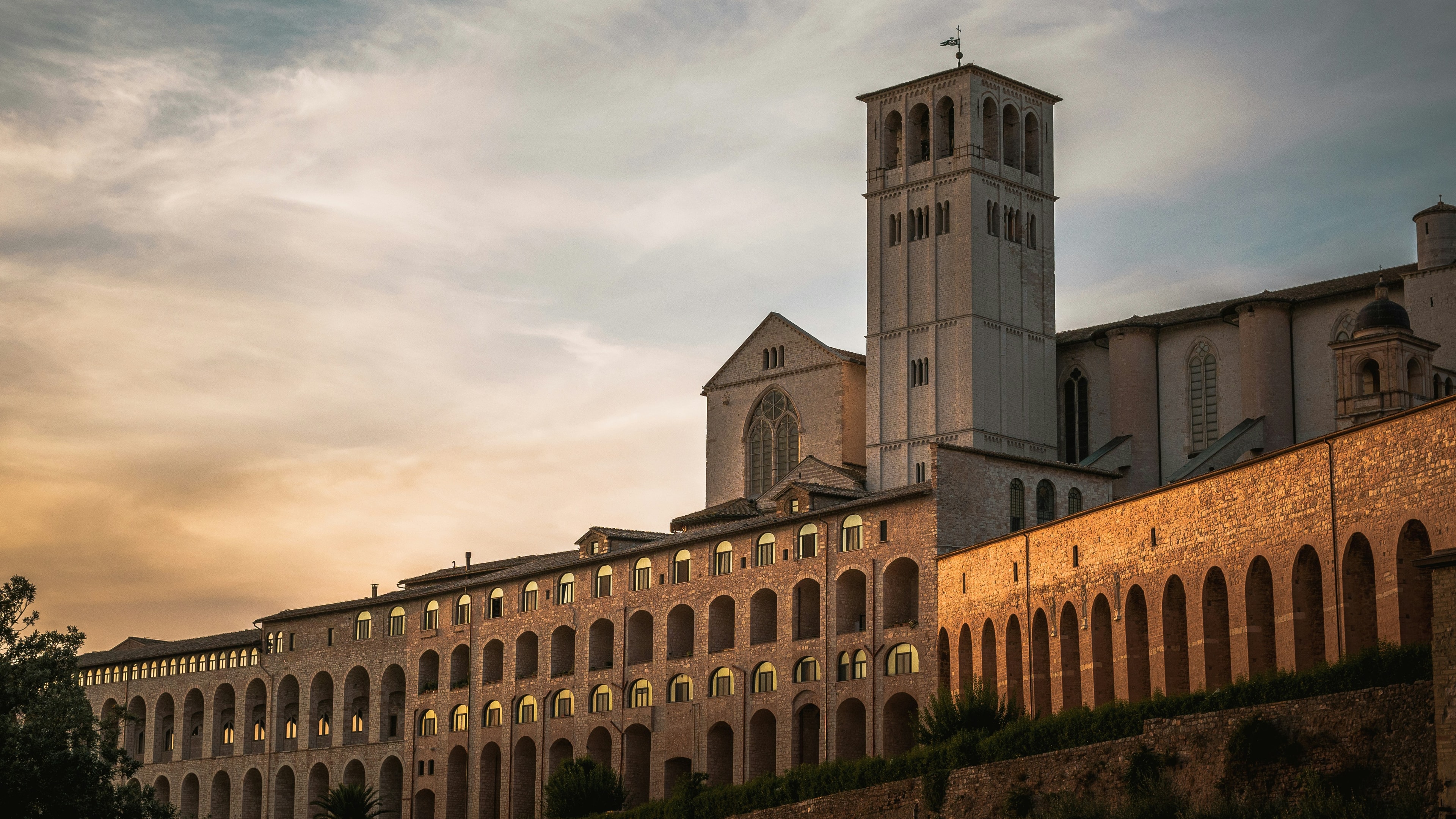 La Basilica di San Francesco e il Sacro Convento di Assisi al tramonto, con le prime finestre illuminate